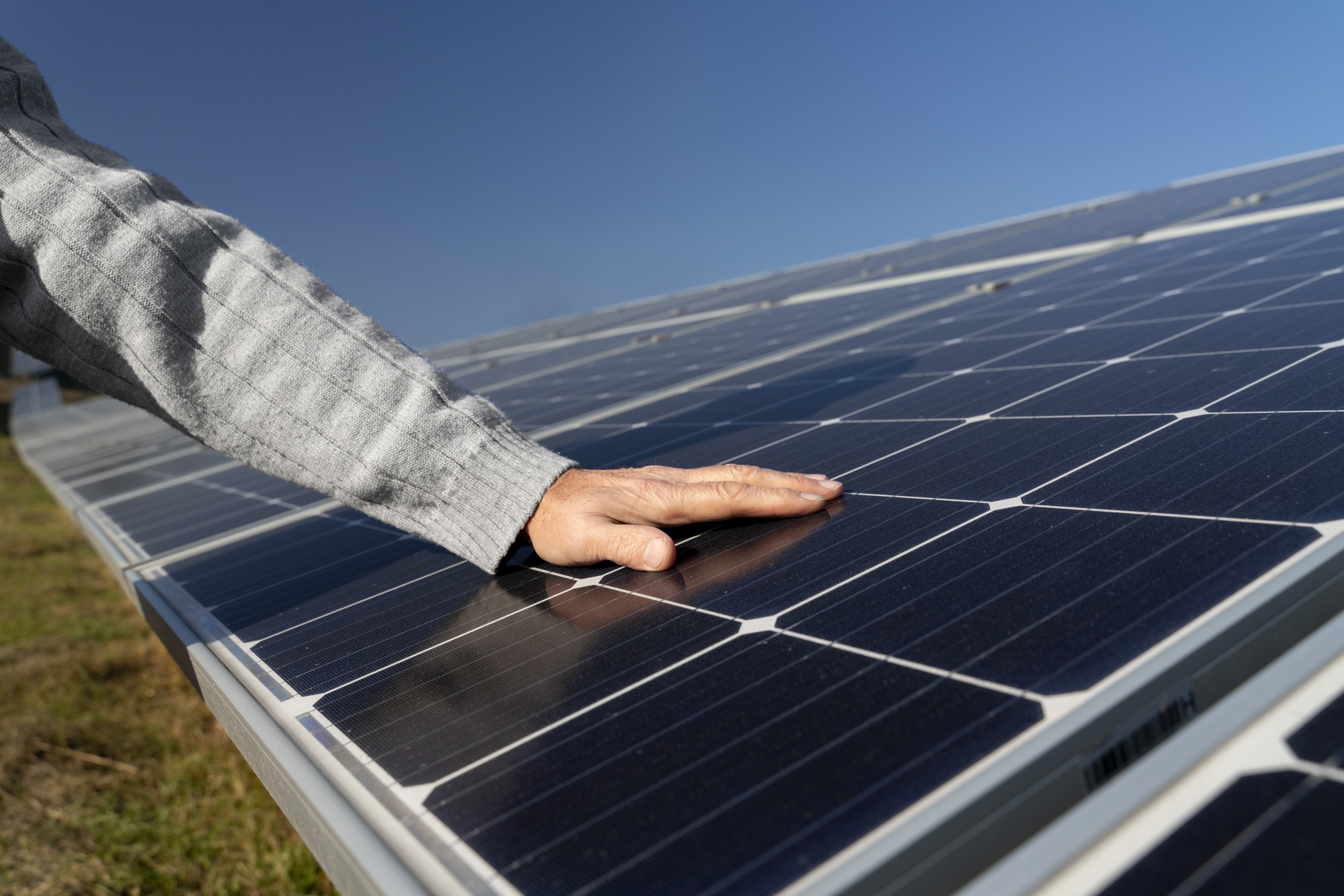 Mão tocando painel solar em campo aberto, representando os desafios e crescimento do setor fotovoltaico no Brasil.